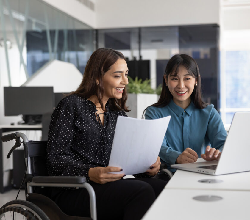 Happy female office employee with disability consulting young Chinese colleague