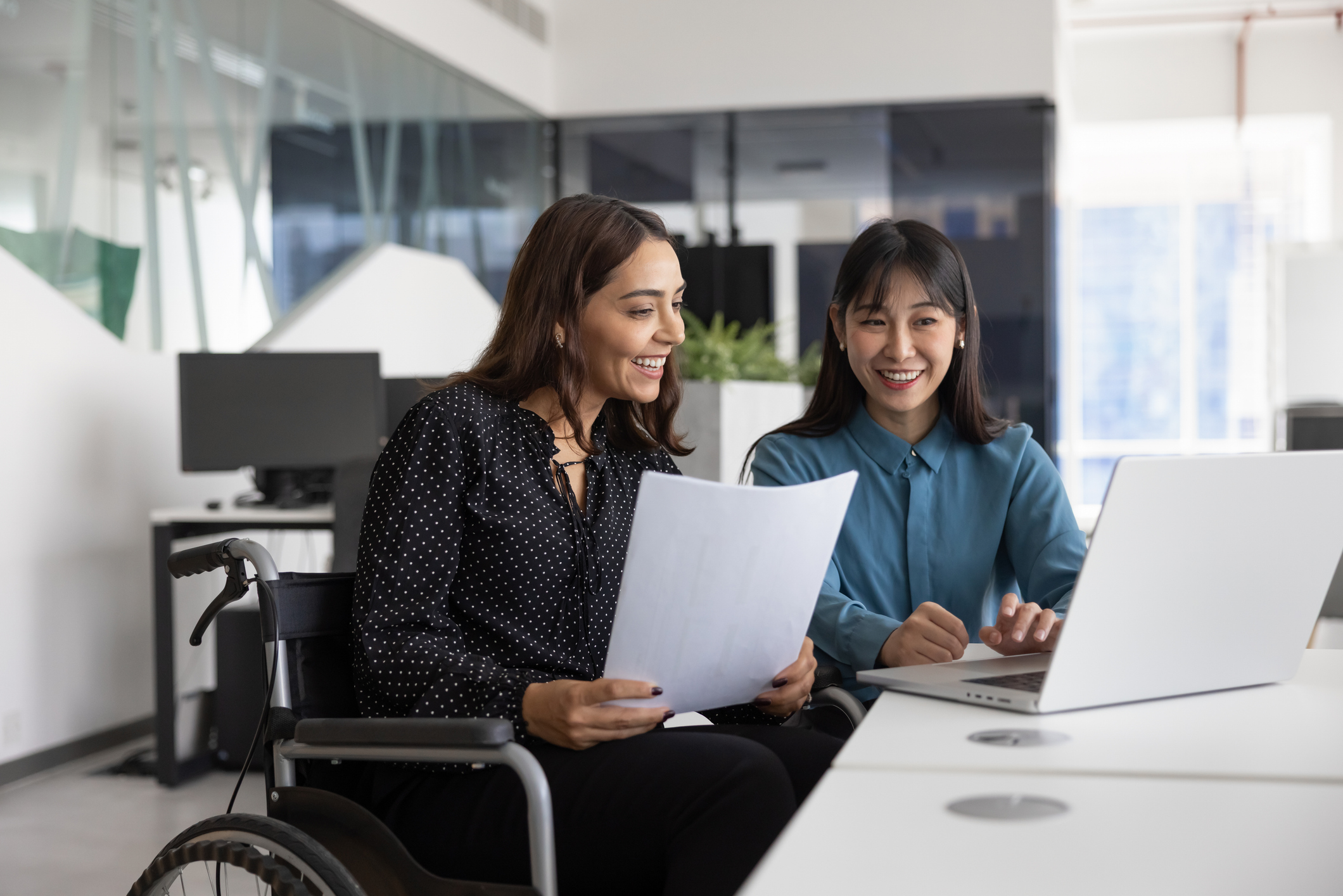 Happy female office employee with disability consulting young Chinese colleague